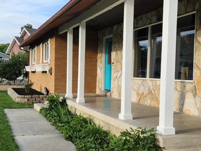 Front entry with stone veneer and brick siding, covered porch, and concrete walkway