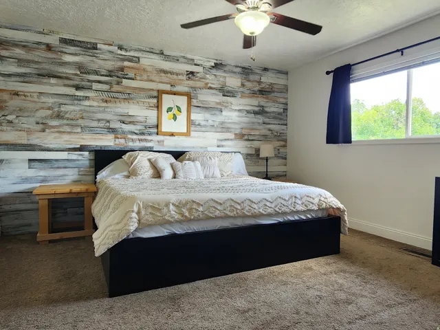 Spacious primary bedroom featuring a shiplap accent wall, ceiling fan with integrated lighting, carpet flooring, and built-in shelving