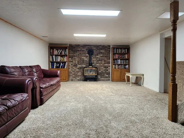 Spacious room featuring carpeting, wood-finish built-in shelving, brick accent wall, and a wood-burning stove