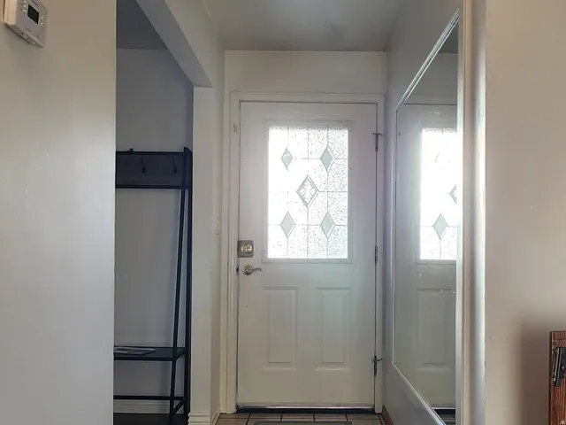 Entryway featuring a white door with decorative glass, light-toned tile flooring, and a full-length wall mirror