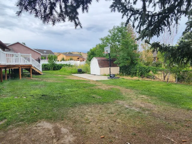 Expansive grassy yard featuring a multi-level wood deck with white railings, a small shed, and a concrete pad