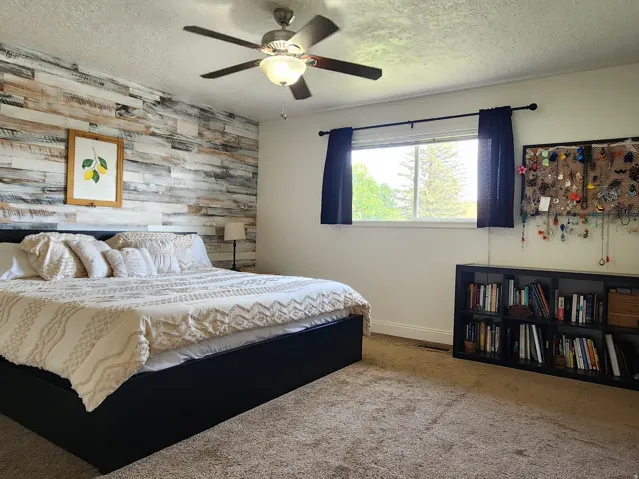 Spacious primary bedroom featuring a shiplap accent wall, ceiling fan with integrated lighting, large windows with blue drapery, and built-in shelving