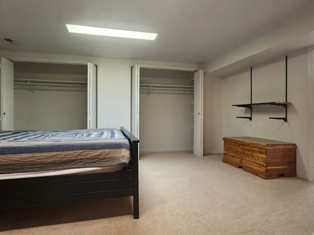 Carpeted room featuring dual bi-fold door closets, recessed lighting, and wall-mounted shelving