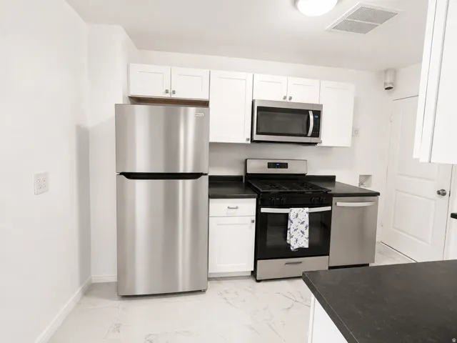 Kitchen featuring white shaker cabinetry, stainless steel appliances, dark countertops, and tile flooring