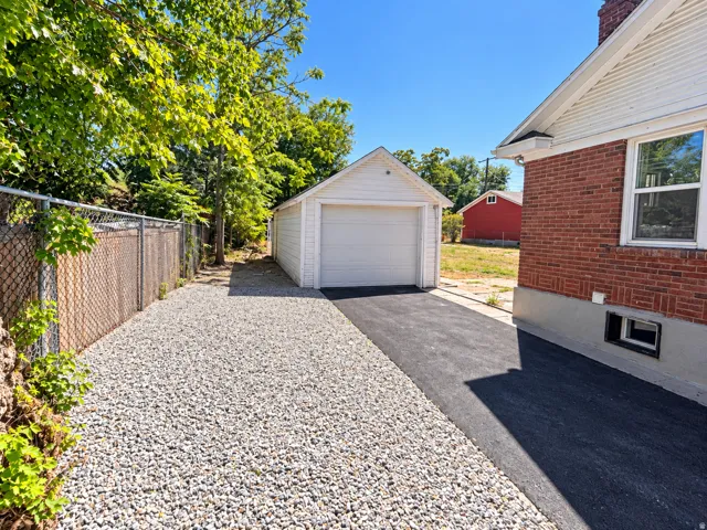 Detached garage with white siding, asphalt driveway, gravel parking area, and red brick exterior