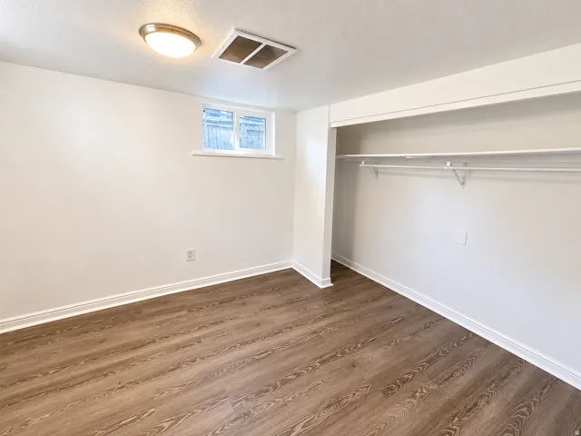 Room featuring wood-finish flooring, white walls, a flush-mount ceiling light, and a built-in closet with shelving and a hanging rod