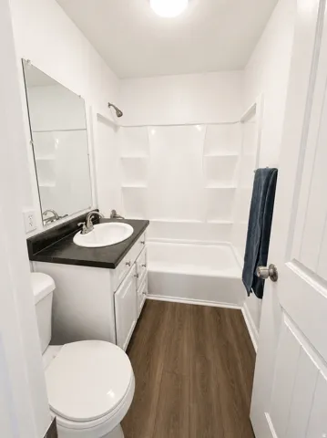 Wood-finish flooring with a white vanity featuring a dark countertop, white drop-in sink, and chrome faucet