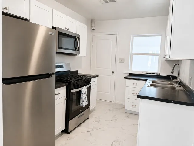 Kitchen featuring white cabinetry, dark countertops, stainless steel appliances, a dual basin sink, and tile flooring