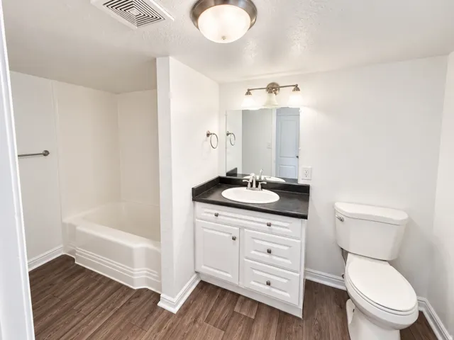 Bathroom featuring a white vanity with dark countertop, an integrated sink, a full-size mirror, and wood-finish flooring