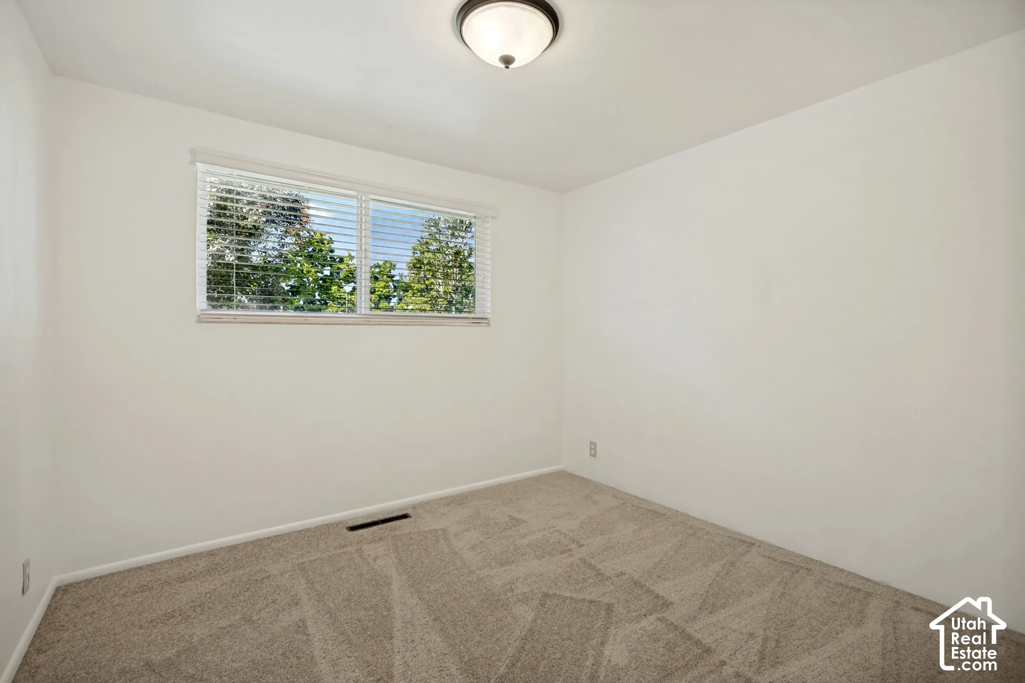 Light-colored walls, patterned carpeting, a window with blinds, and a flush-mount ceiling light fixture