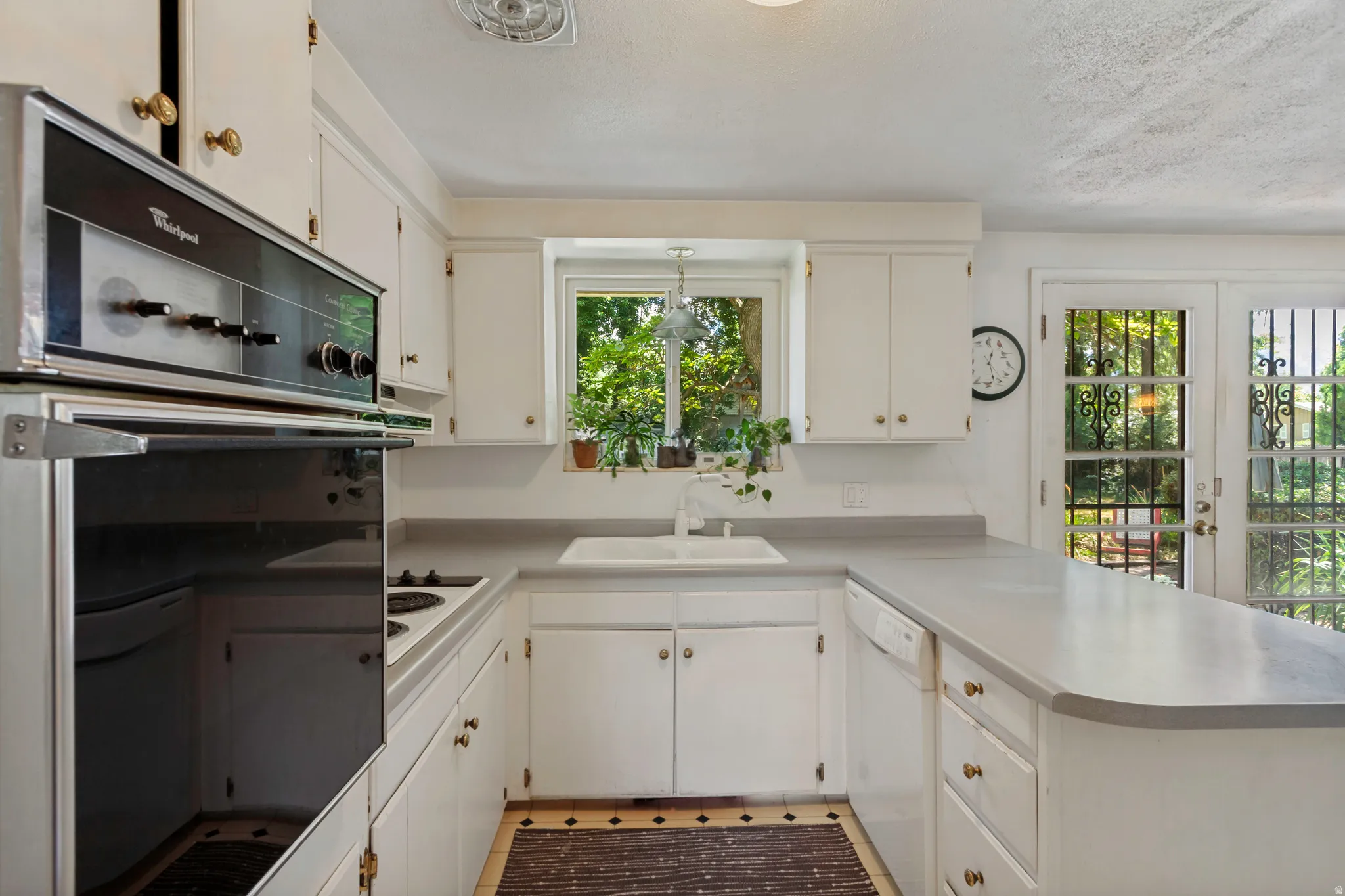 White cabinetry with gold-tone hardware, built-in wall oven, under-mount sink, and dual glass-paneled doors with decorative grilles