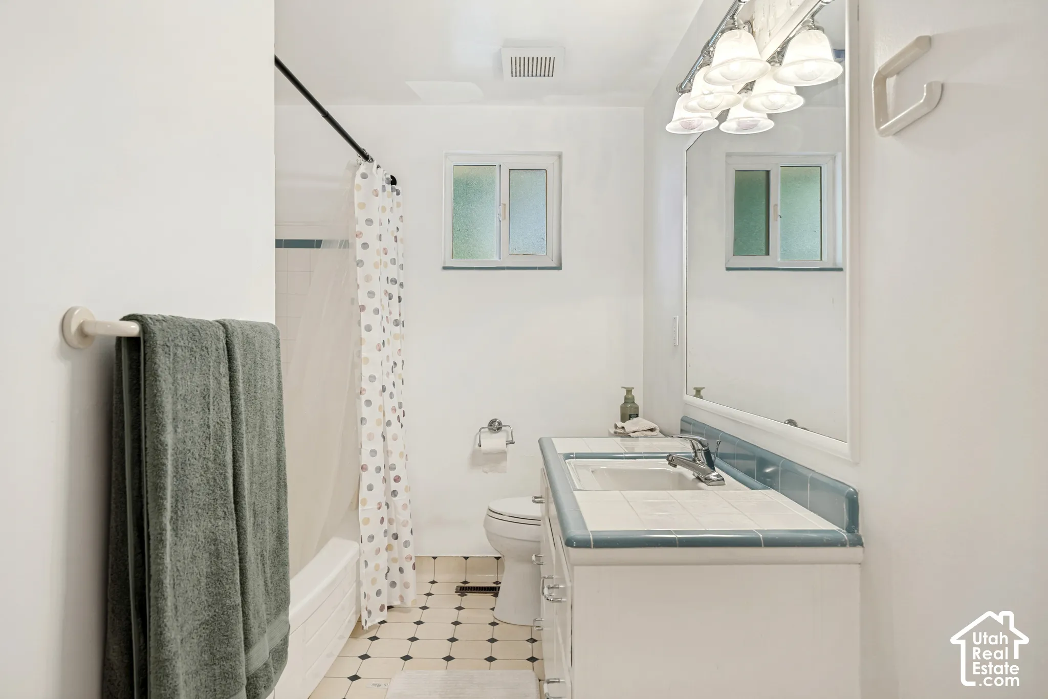 Bathroom featuring a vanity with dual sinks, overhead lighting, tiled countertop, and an enclosed shower