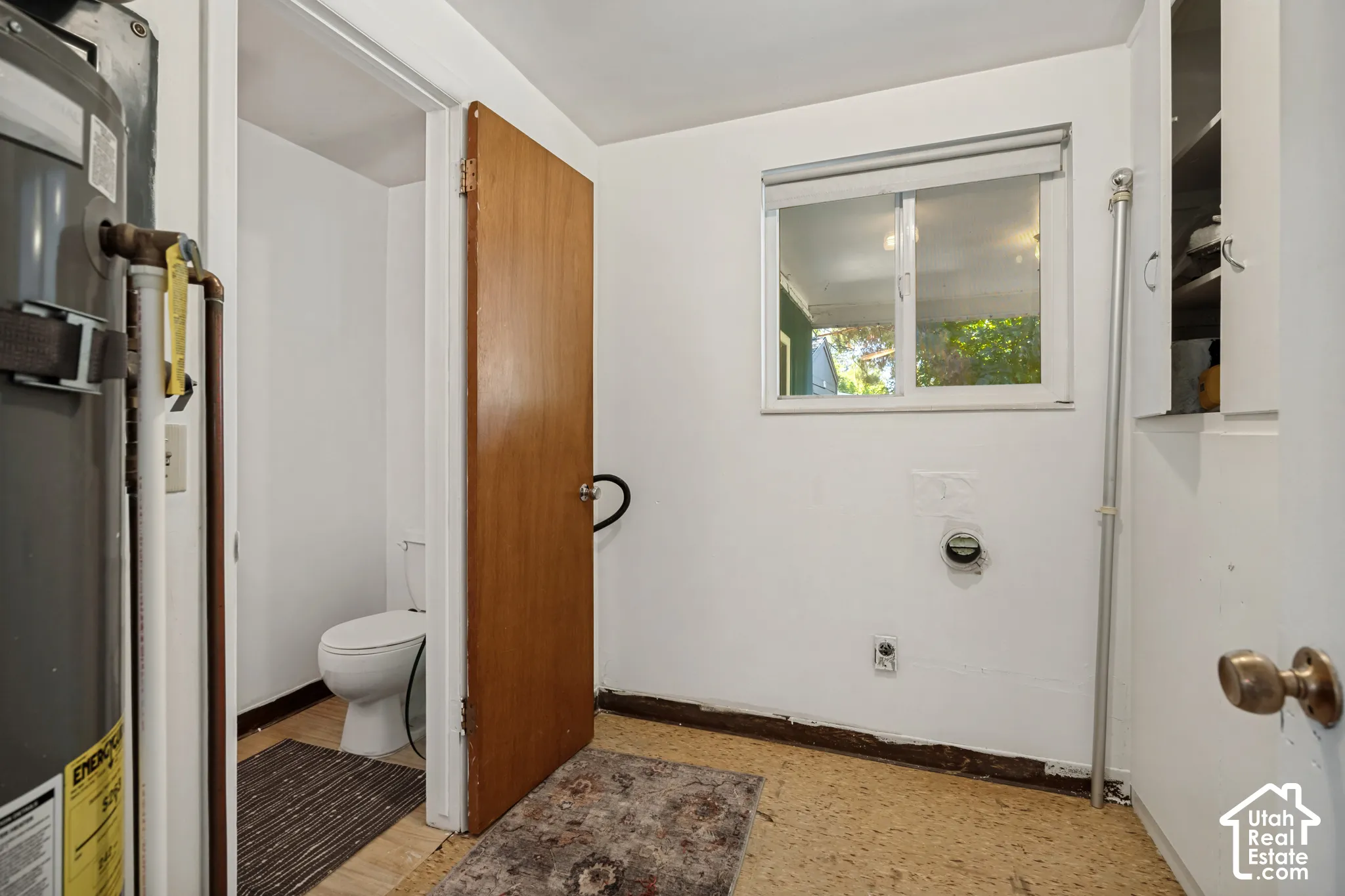 White walls, window with roller shade, built-in storage cabinet, and a water heater