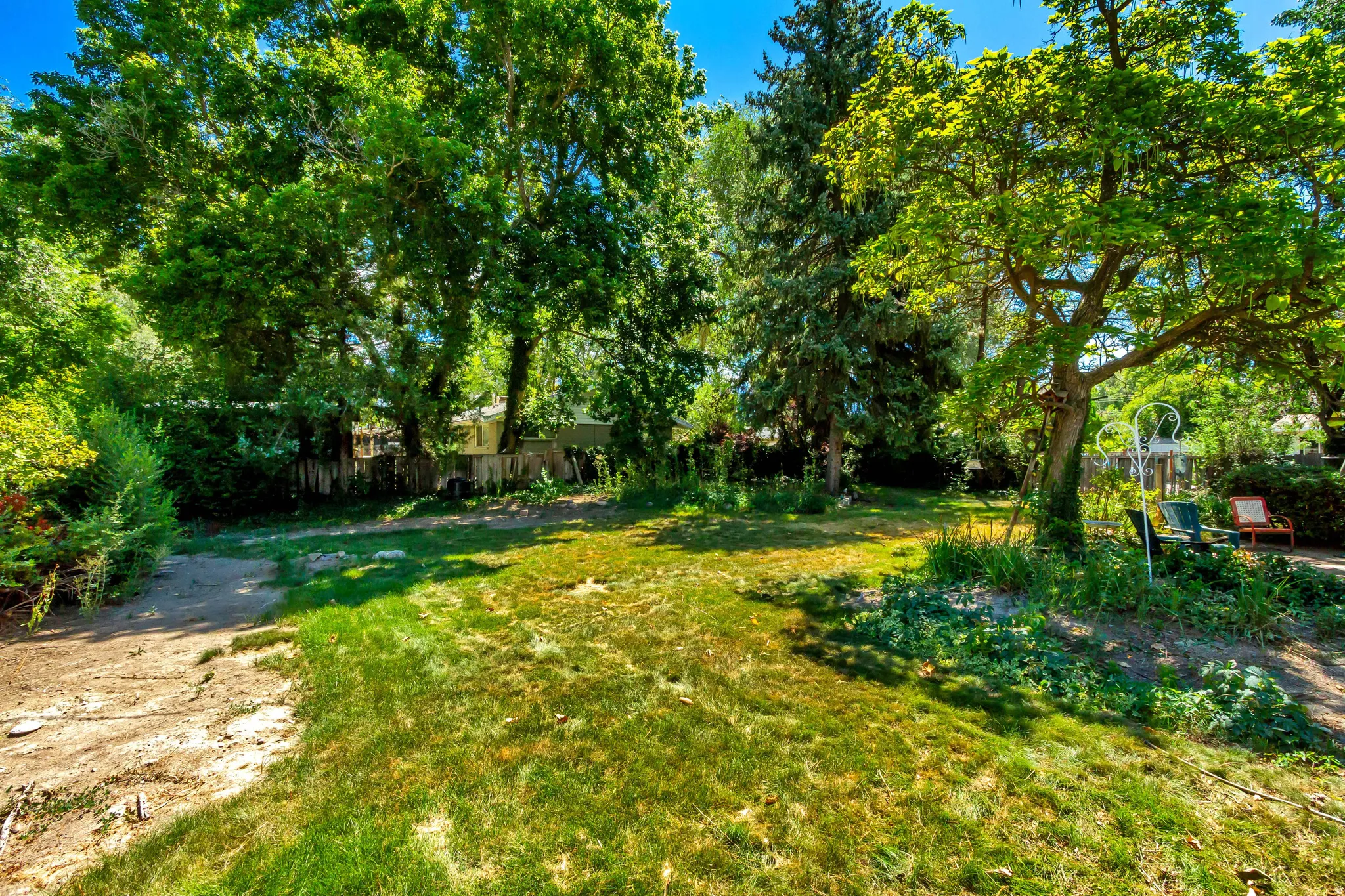 Expansive rear yard featuring mature trees, established landscaping, and a partial privacy fence