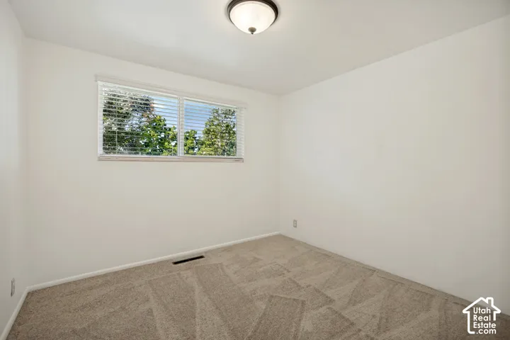 Light-colored walls, patterned carpeting, a window with blinds, and a flush-mount ceiling light fixture