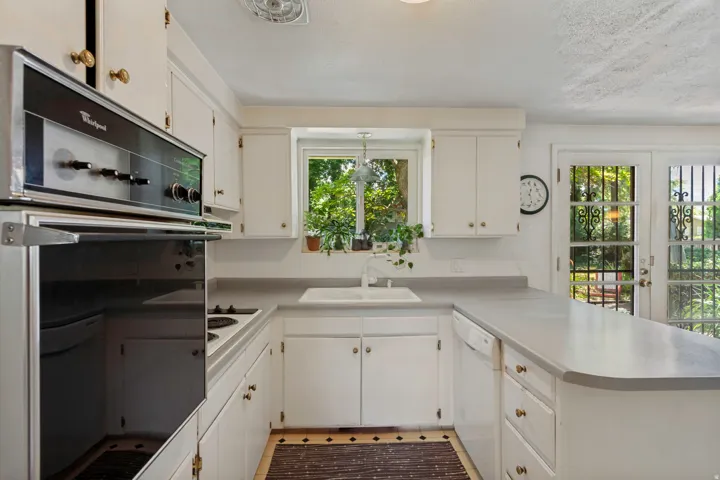 White cabinetry with gold-tone hardware, built-in wall oven, under-mount sink, and dual glass-paneled doors with decorative grilles
