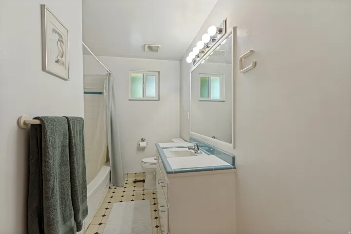 Bathroom featuring a built-in vanity with dual sinks, overhead vanity lighting, a large mirror, a window, and patterned floor tiling