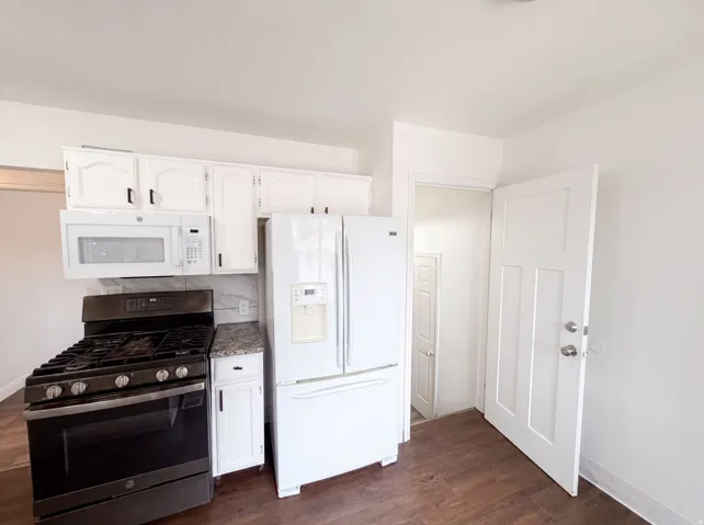 Full kitchen featuring a gas range, over-the-range microwave, side-by-side refrigerator, white cabinetry, and wood-finish flooring