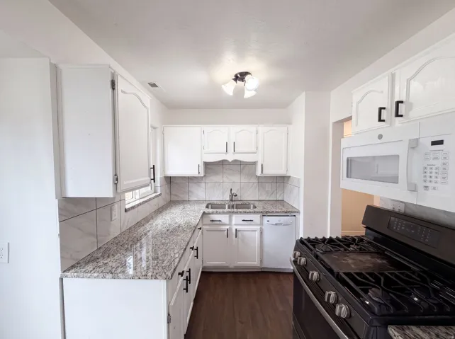 White cabinetry with matte black hardware, granite-style countertops, tile backsplash, stainless steel sink, and wood-finish flooring