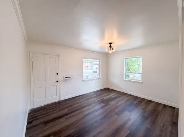 Wood-finish flooring, white walls, two windows, crown molding, and a five-bulb ceiling fixture