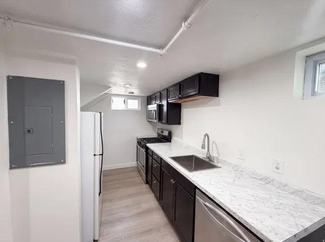 Kitchen featuring dark-finish cabinetry, light-finish countertops, stainless steel appliances, a stainless steel sink, and wood-finish flooring