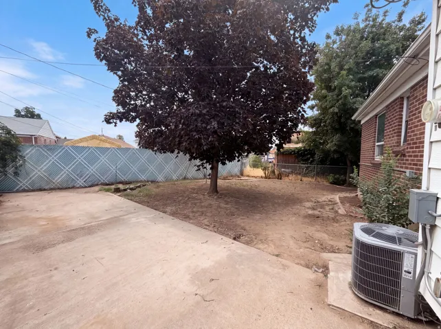 Expansive yard space featuring a mature tree, concrete patio area, brick exterior, and a chain-link fence with privacy screening