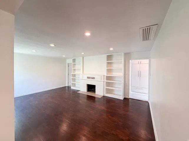 Recessed lighting, wood-finish flooring, built-in shelving, brick fireplace surround, and built-in white cabinetry