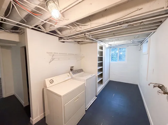 Laundry area featuring exposed ceiling joists, overhead lighting, a washer and dryer, built-in shelving, and a window
