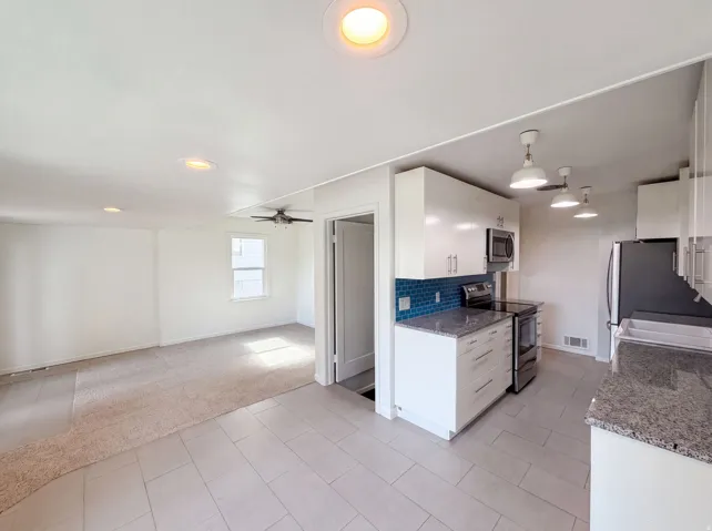 Bright kitchen with white cabinetry, blue tile backsplash, stainless steel appliances, and light-toned tile flooring