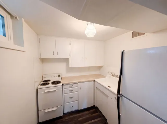 Compact kitchen featuring white cabinetry, light-toned countertops, a white range, a refrigerator, and wood-finish flooring