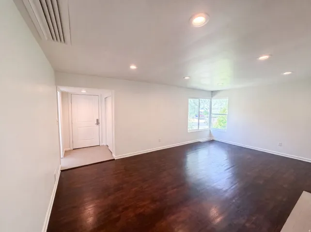 Recessed ceiling lighting, wood-finish flooring, white walls, and a corner window arrangement