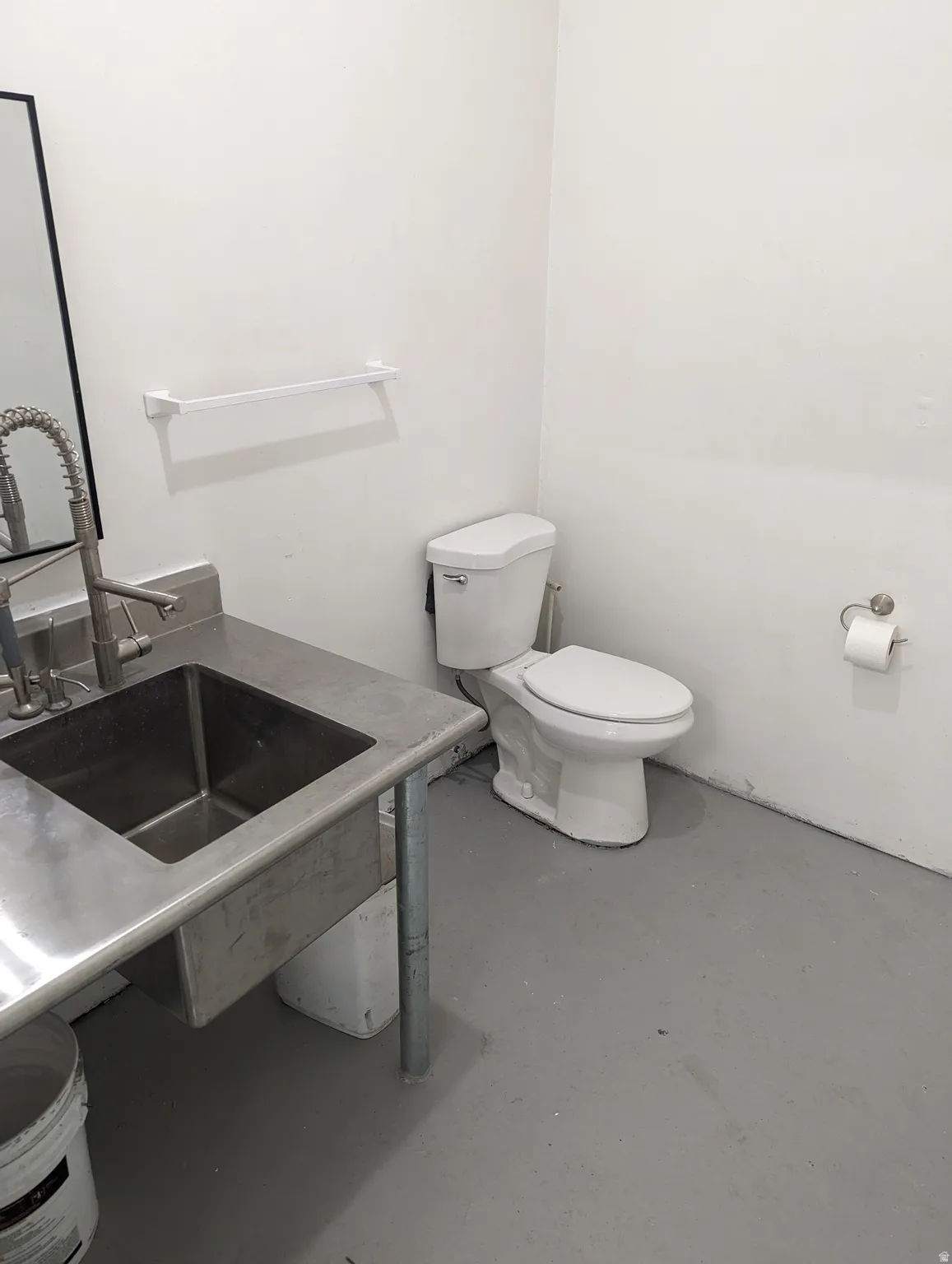 White walls, gray flooring, stainless steel sink with gooseneck faucet, and white toilet