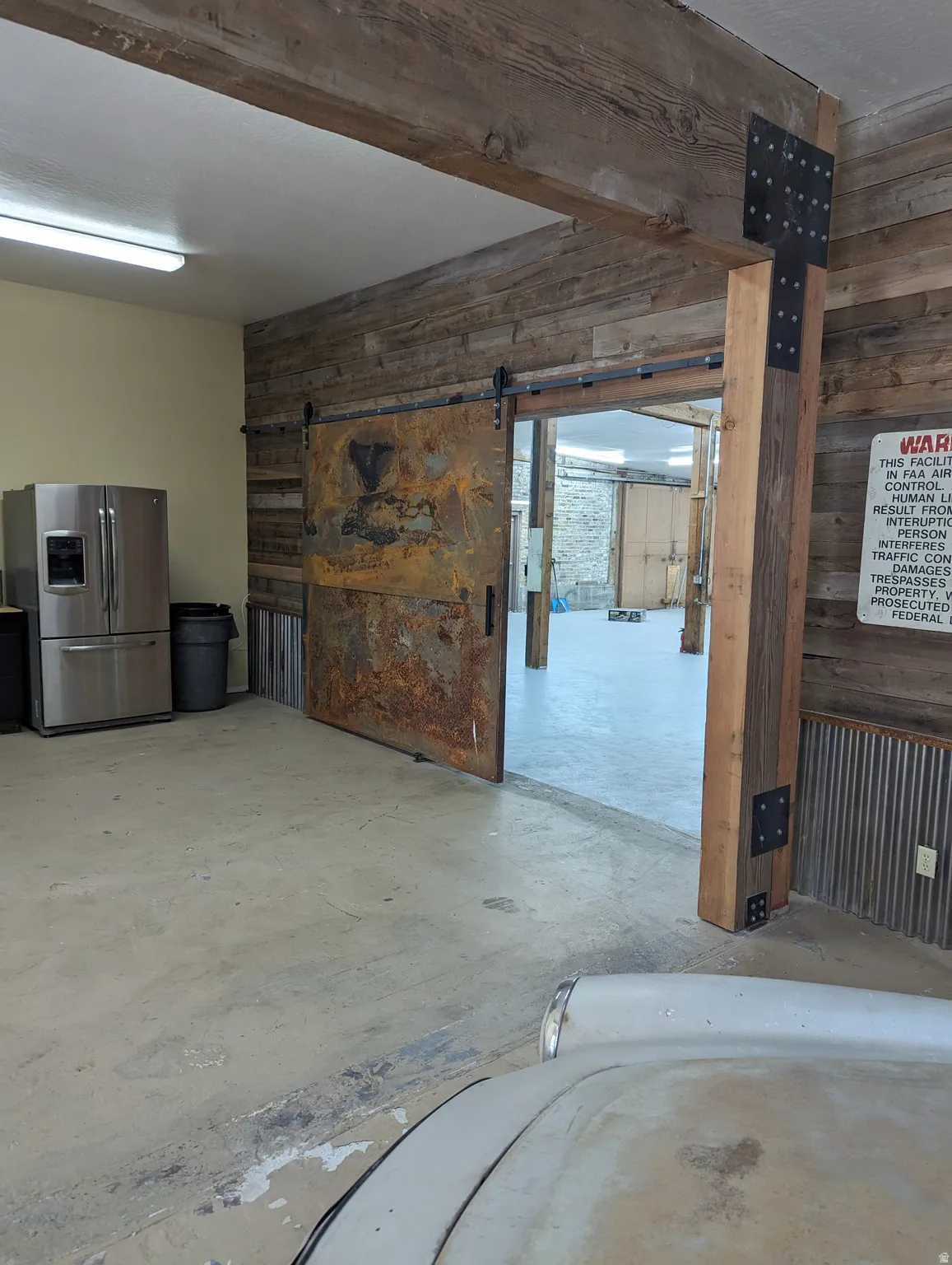 Concrete flooring, wood plank wall finishes, exposed wood beam ceiling, and a rustic metal barn door