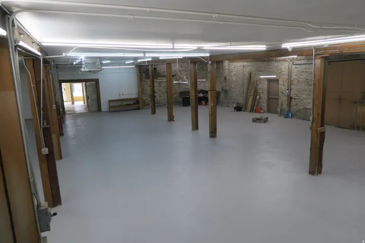 Spacious interior with light gray flooring, exposed brick wall, and multiple support beams