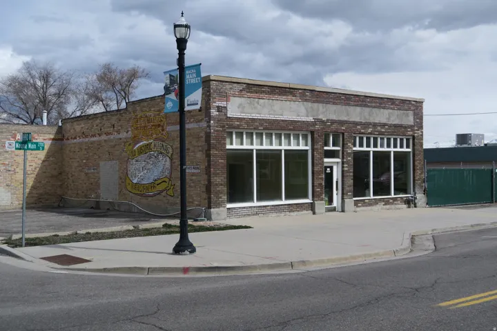Brick facade commercial building with prominent storefront windows, a corner sidewalk, and street frontage