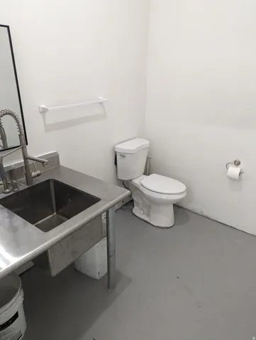 White walls, gray flooring, stainless steel sink with gooseneck faucet, and white toilet