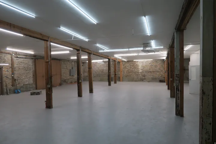Expansive open space featuring exposed brick walls, numerous wood support columns, and a smooth light-colored floor