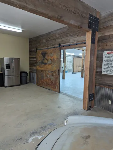 Concrete flooring, wood plank wall finishes, exposed wood beam ceiling, and a rustic metal barn door