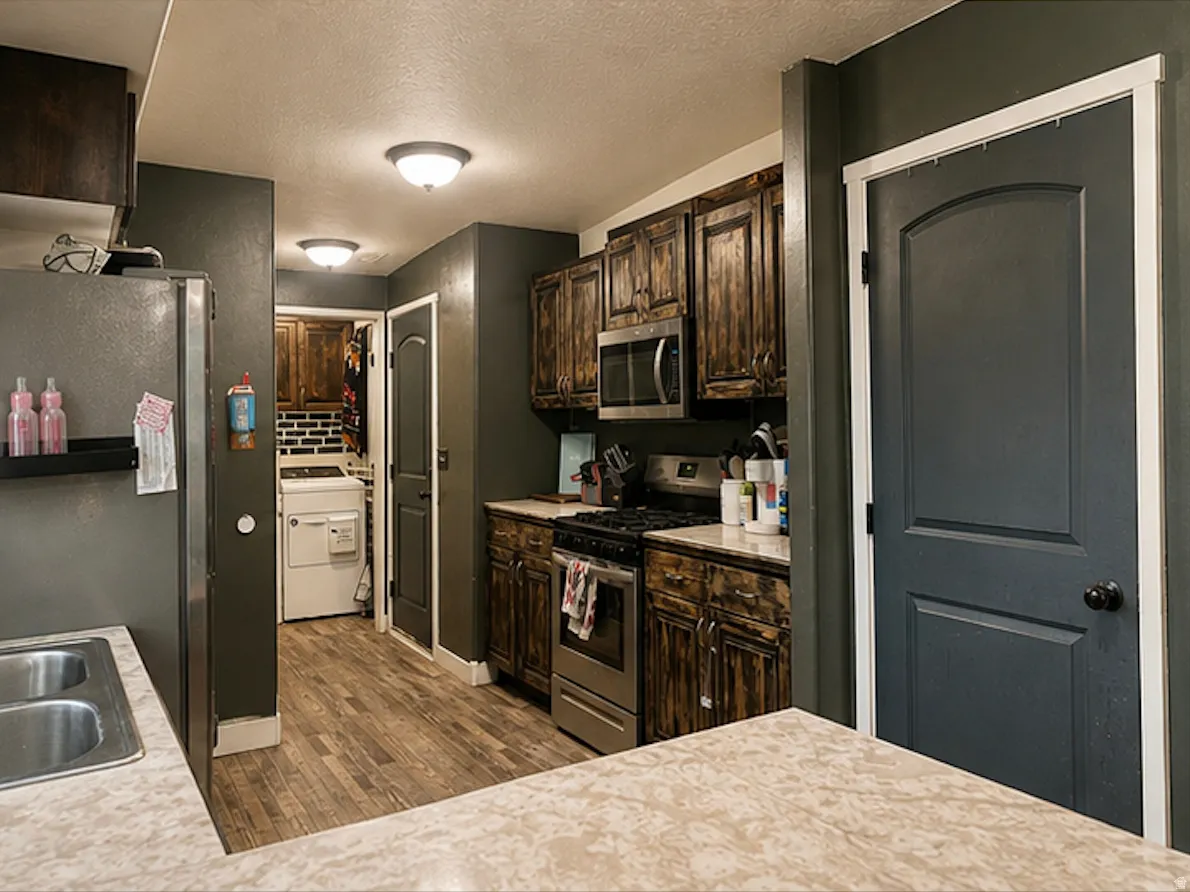 Kitchen featuring wood-finish flooring, dark wood cabinetry, stainless steel appliances, and solid surface countertops