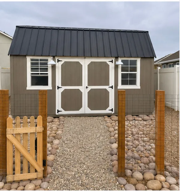 Storage shed featuring a dark metal roof, dual white barn doors, and two exterior light fixtures