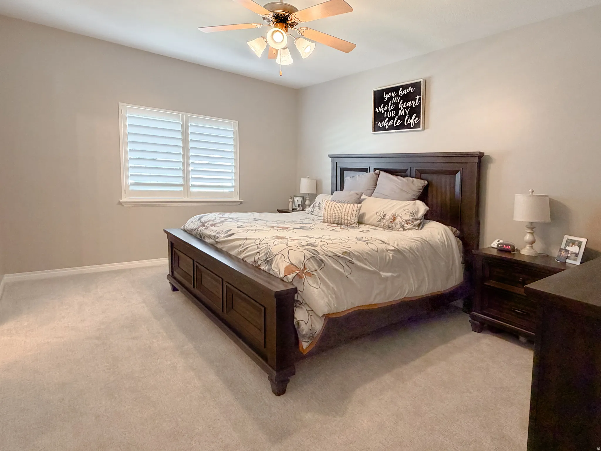 Carpeted flooring, window with plantation shutters, ceiling fan with light fixture, and neutral wall tones