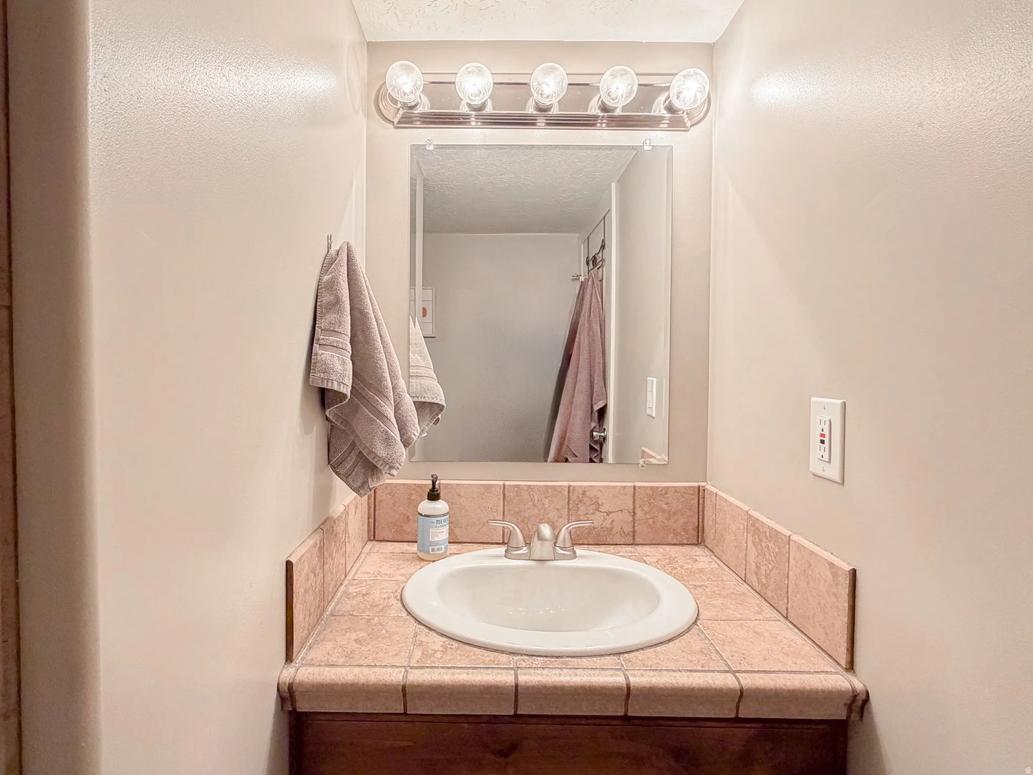 Vanity with tile countertop, integrated sink, and wood-finish cabinetry