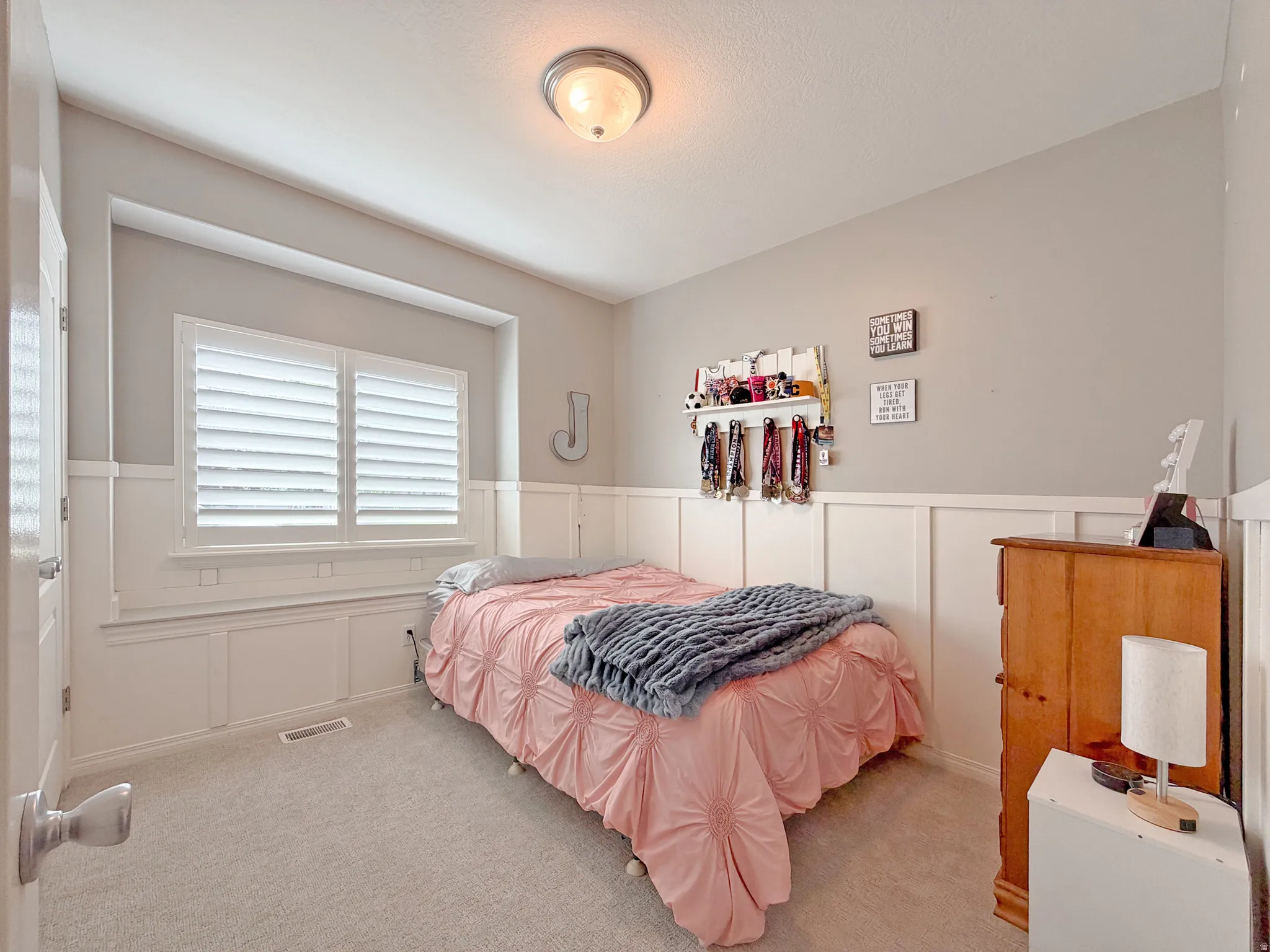 Plush carpet flooring, board and batten wall detailing, window with white plantation shutters, and a ceiling-mounted light fixture
