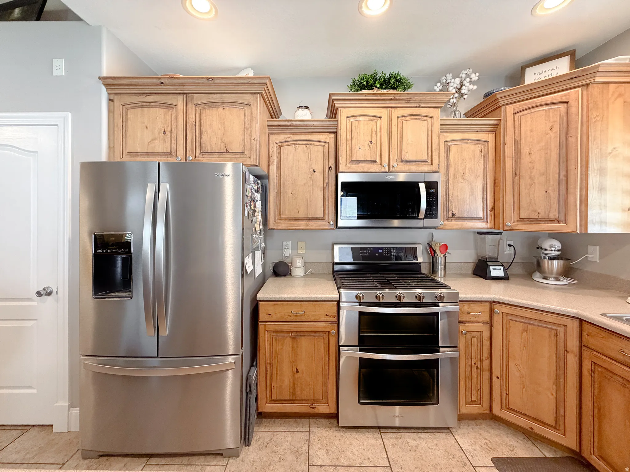 Stainless steel French door refrigerator, built-in microwave, gas range with double ovens, light-toned wood cabinetry, and neutral countertops