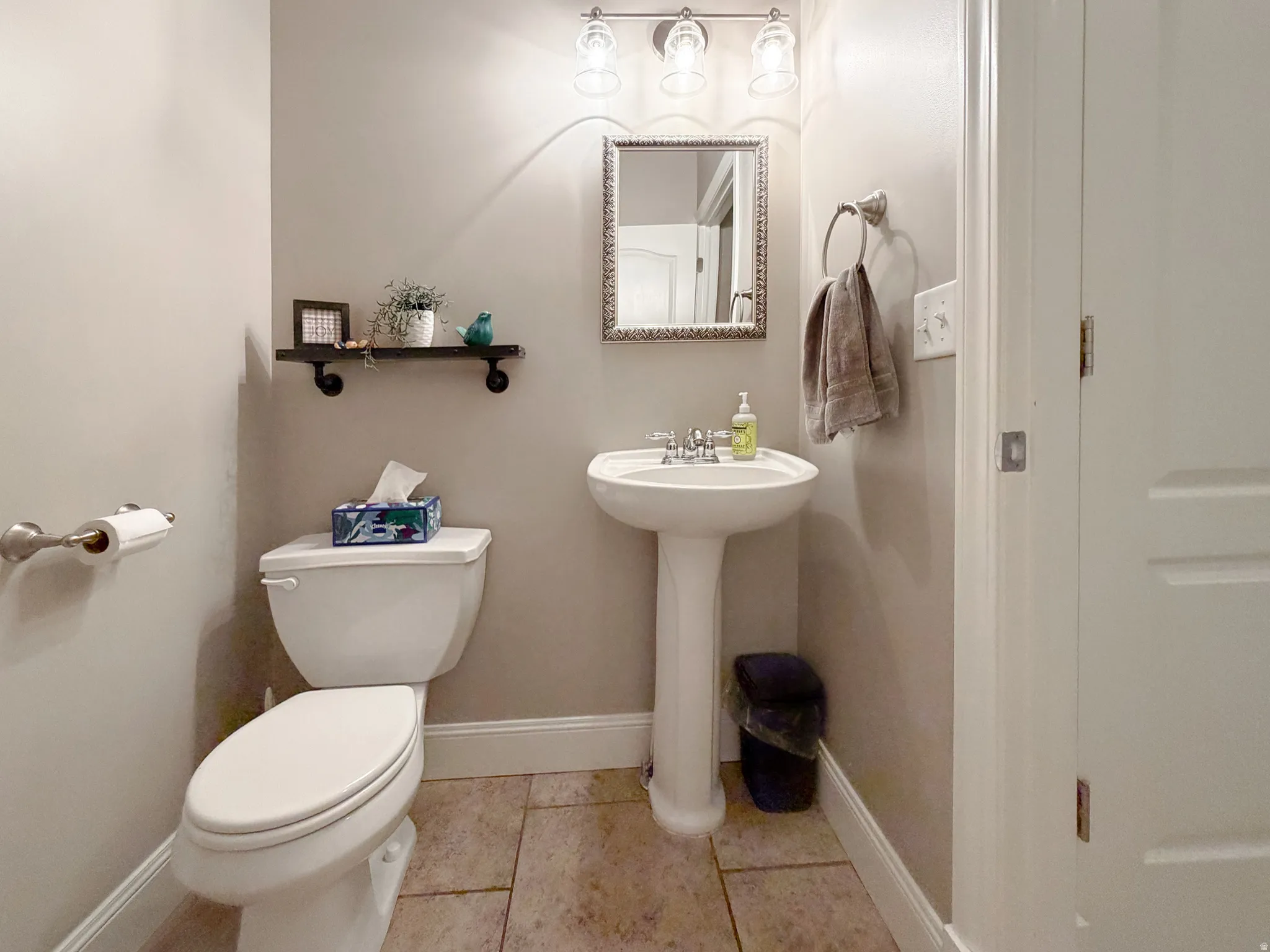 Pedestal sink with chrome faucet, wall-mounted light fixture, decorative mirror, and neutral wall paint