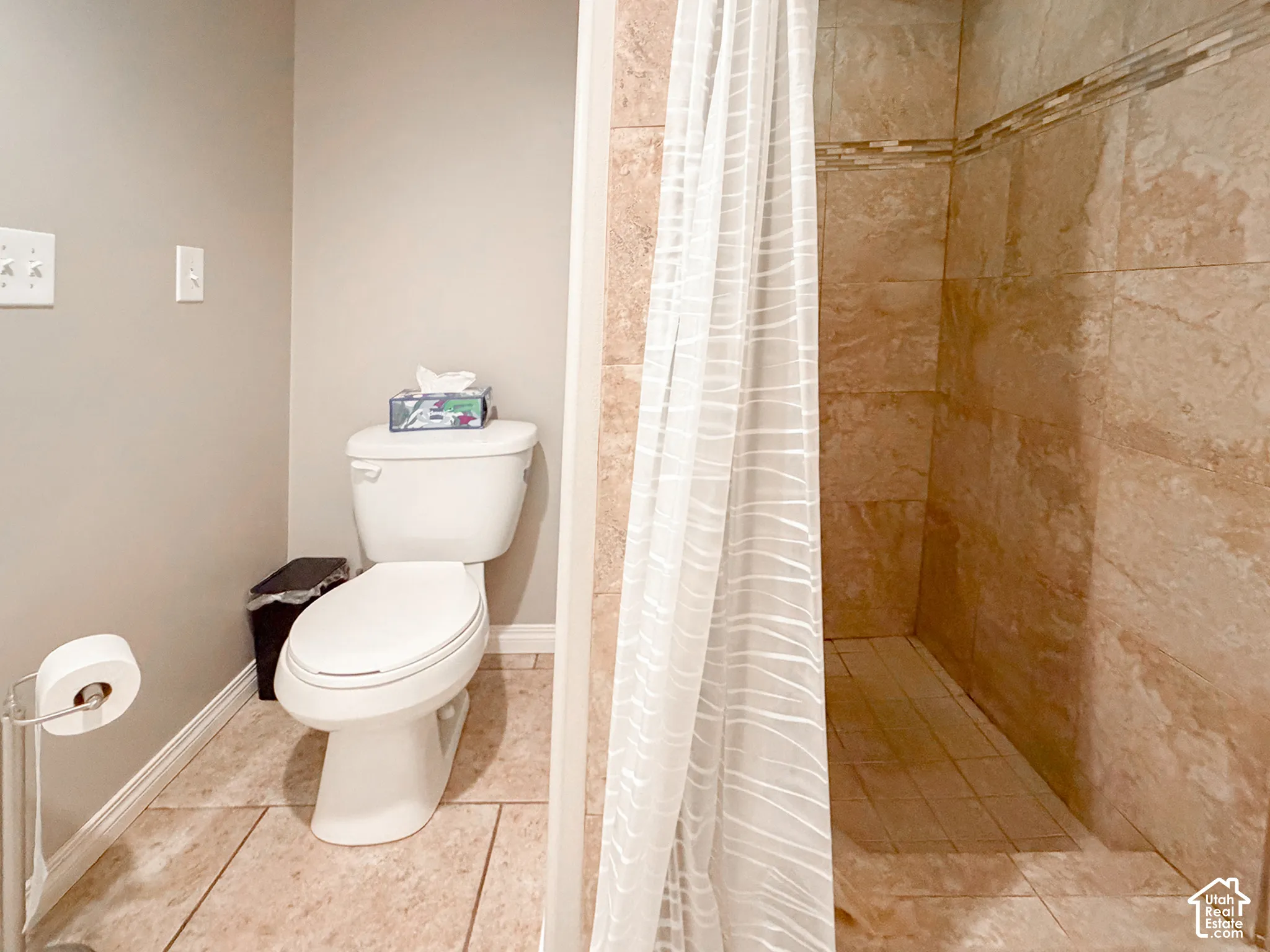 Walk-in shower with tiled walls and decorative accent band, tiled flooring, and a standard toilet