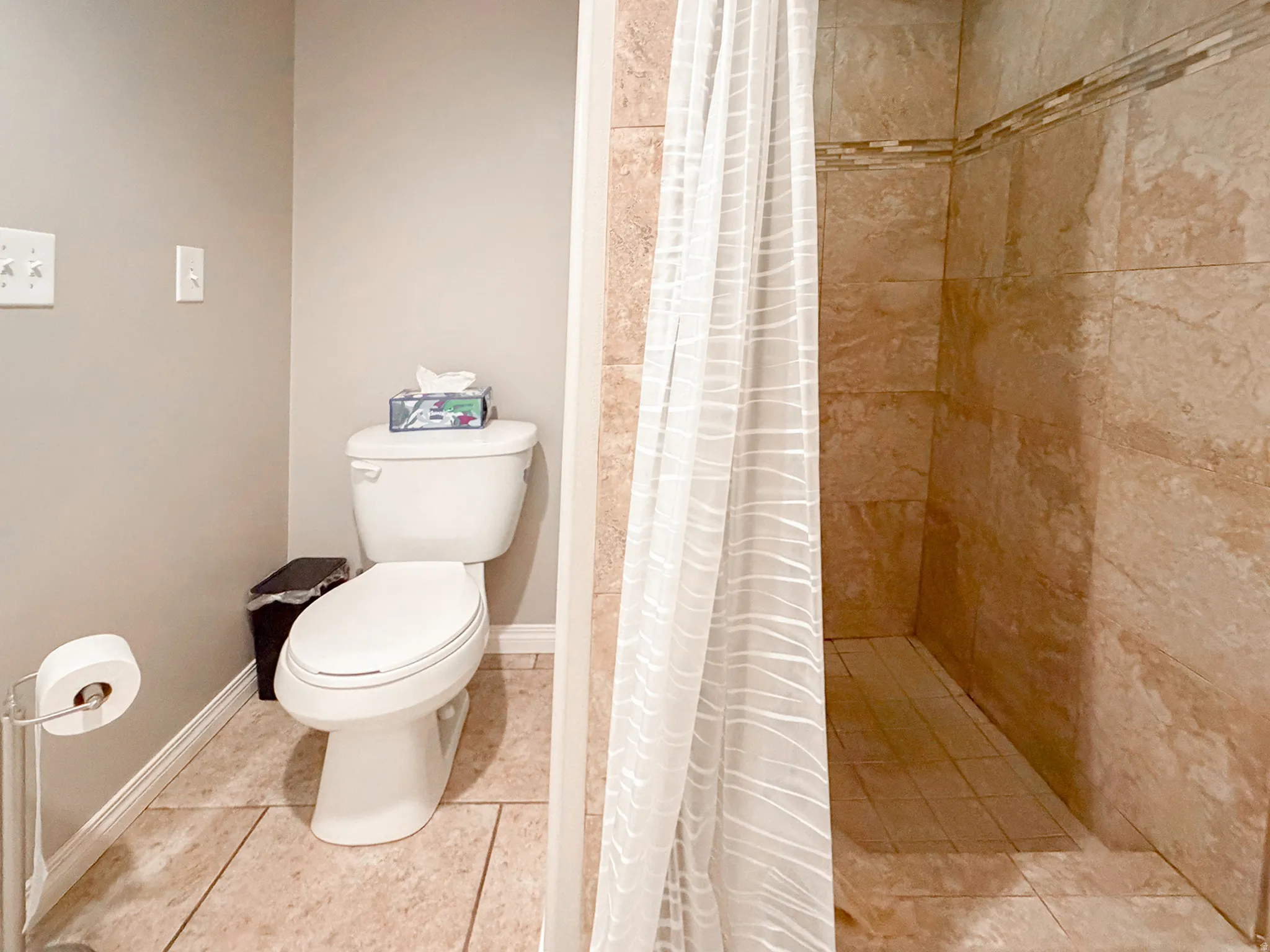 Walk-in shower with tiled walls and decorative accent band, tiled flooring, and a standard toilet