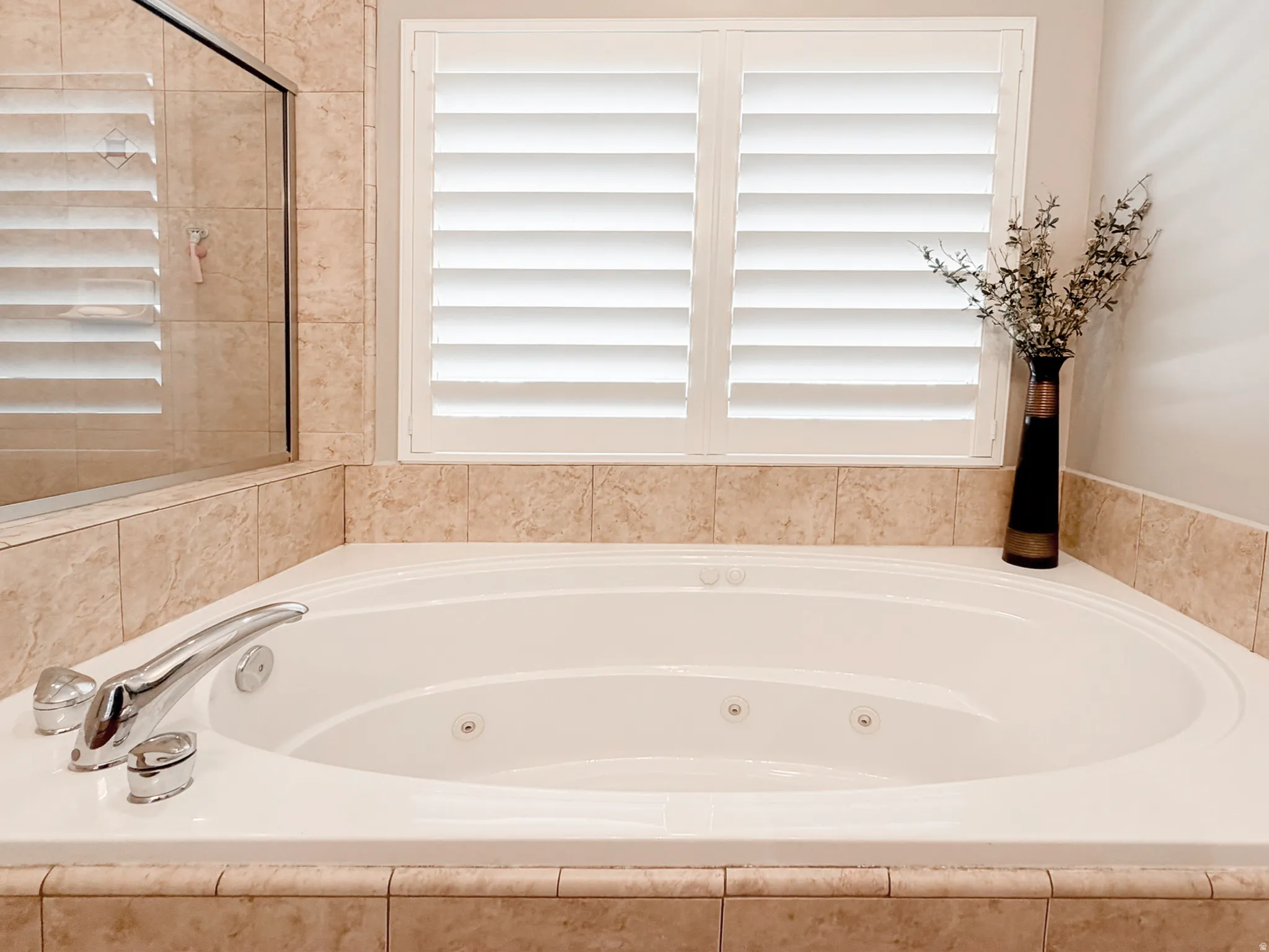 Soaking tub with integrated jets, chrome fixtures, tiled surround, and white louvered shutters