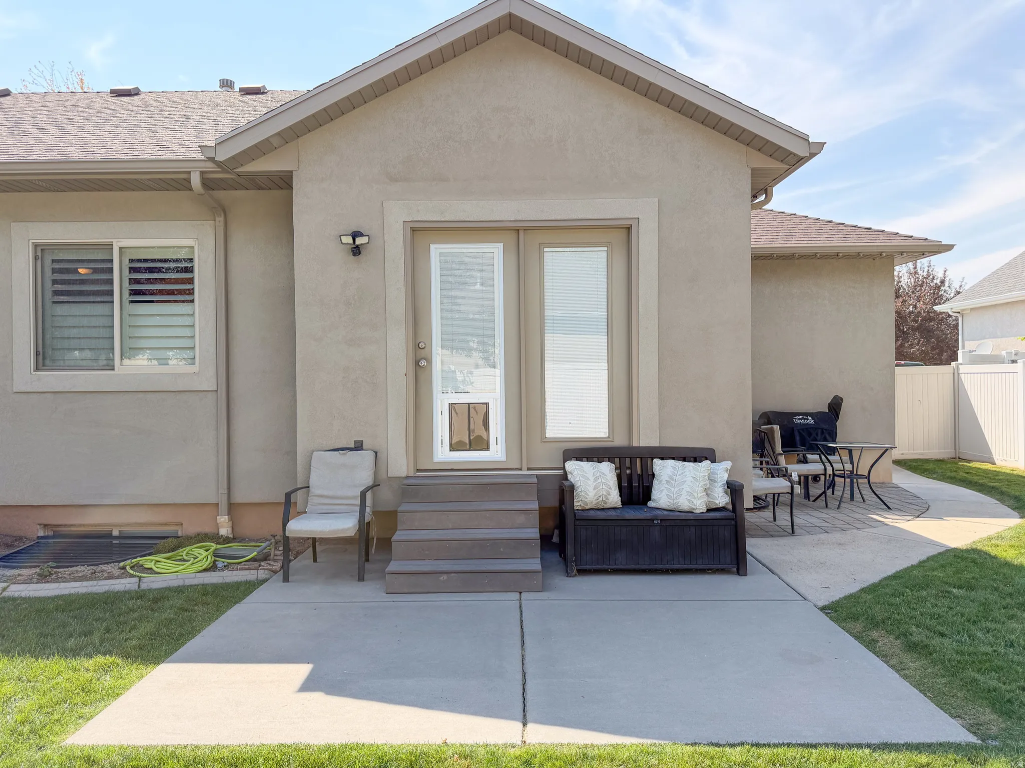 Exterior stucco finish, composite shingle roof, concrete patio, composite steps, and a glass-paneled exterior door