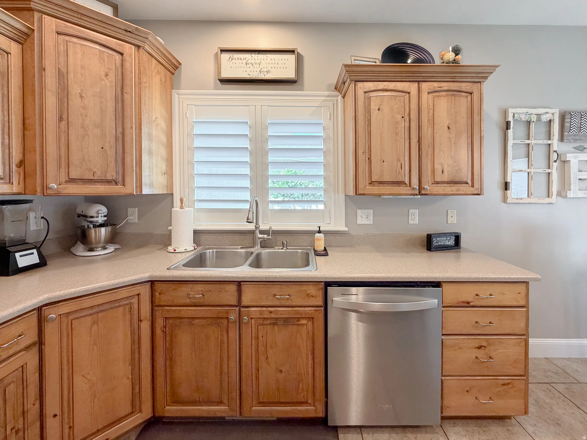 Wood-finish cabinetry with crown molding, double basin stainless steel sink with a gooseneck faucet, light-toned countertop, and a stainless steel dishwasher